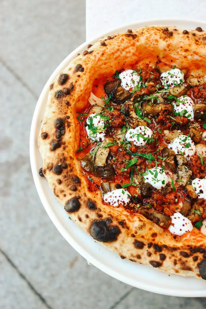 Close-up of a gourmet pizza with cheese, mushrooms, herbs, and tomato sauce.